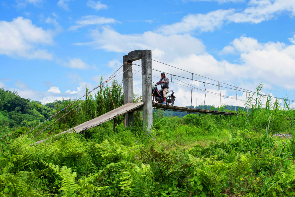 A motorcycle driver navigates the narrow precarious hanging bridge.